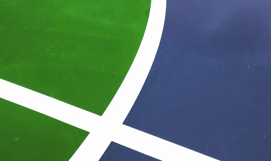 A full-view outdoor basketball court with professional-grade green and blue sports flooring in a UAE residential complex, featuring a FIBA-standard backstop and palm trees.